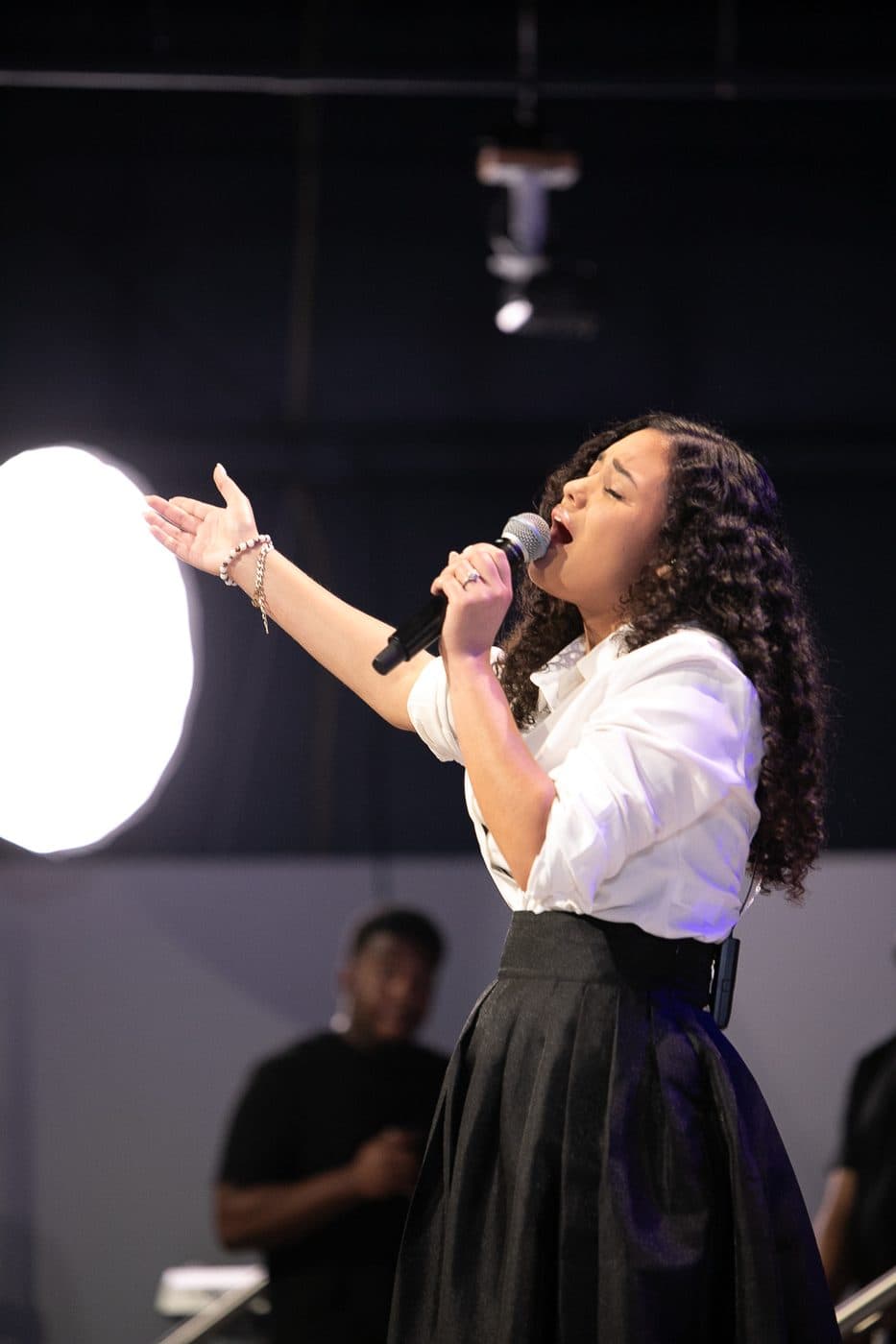 Elizabet María cantando con el brazo extendido en adoración